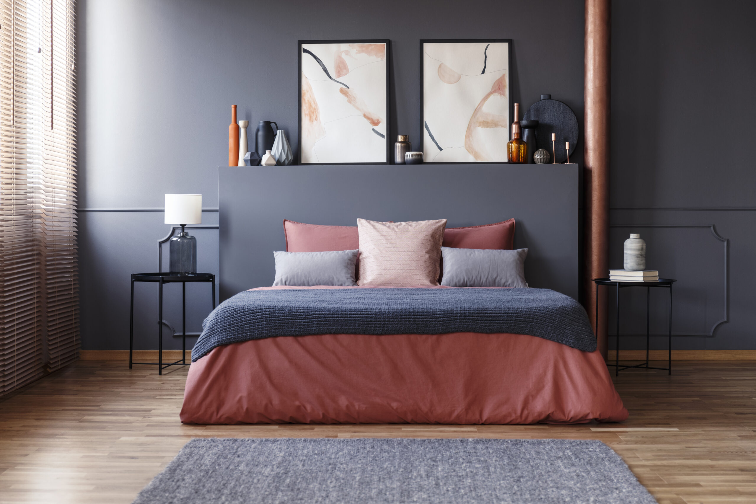 Grey blanket on pink bed in hotel bedroom interior with carpet and poster on headboard