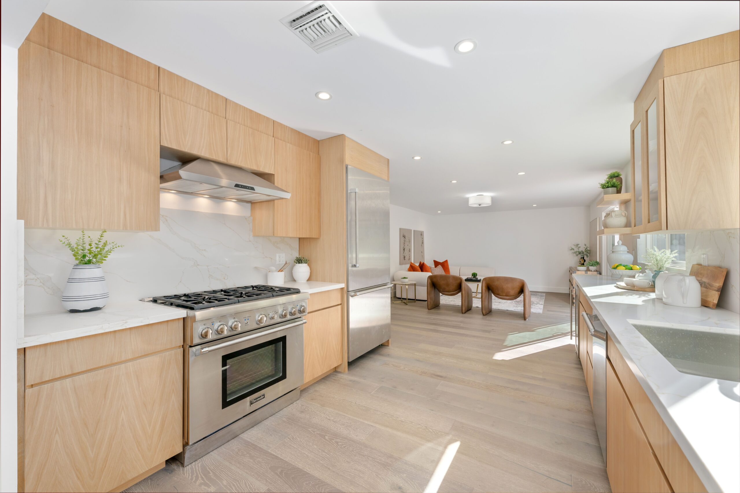 Modern kitchen with wooden cabinets, stainless steel appliances, and open living area, featuring natural light and minimalist decor.