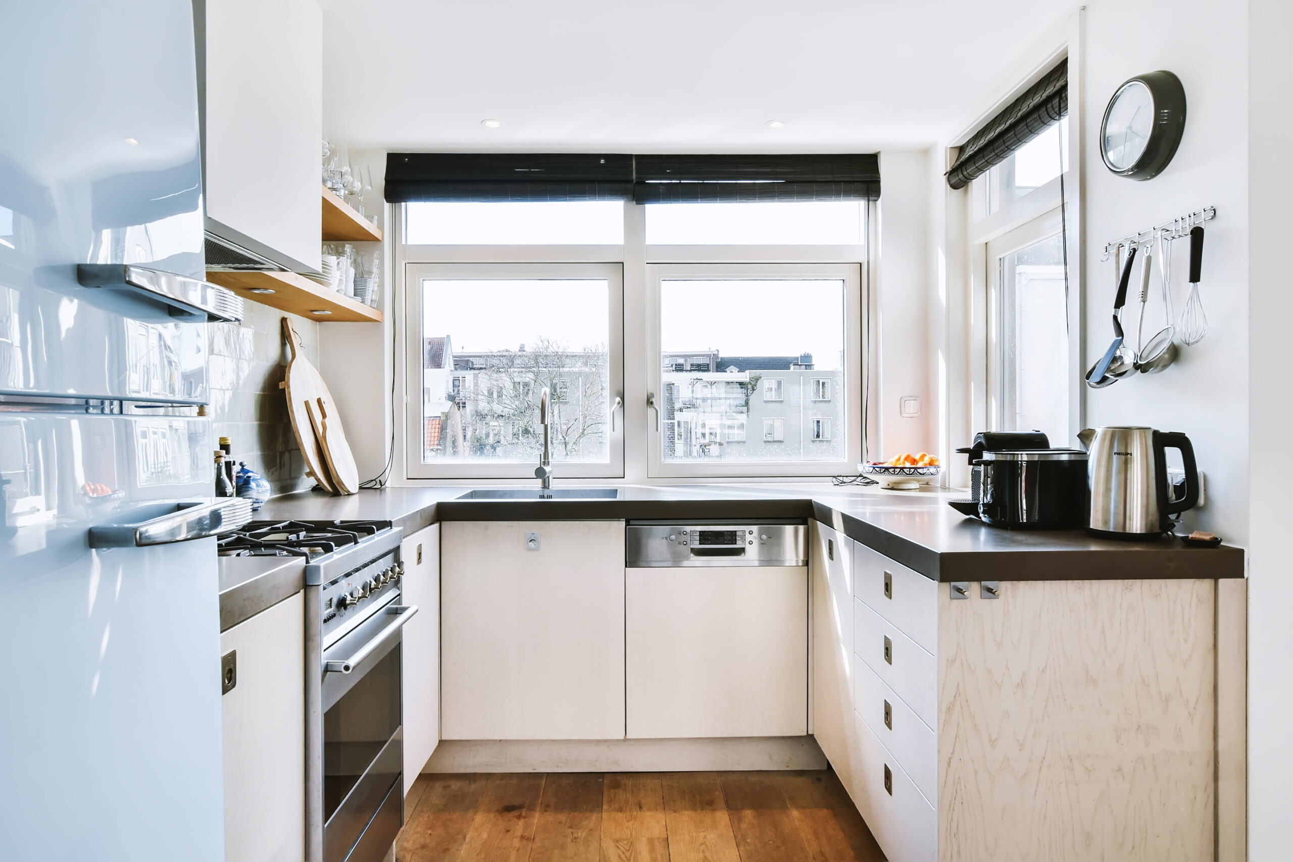 Well organized small home kitchen interior with sink under window and light furniture with stove and fridge in urban apartment