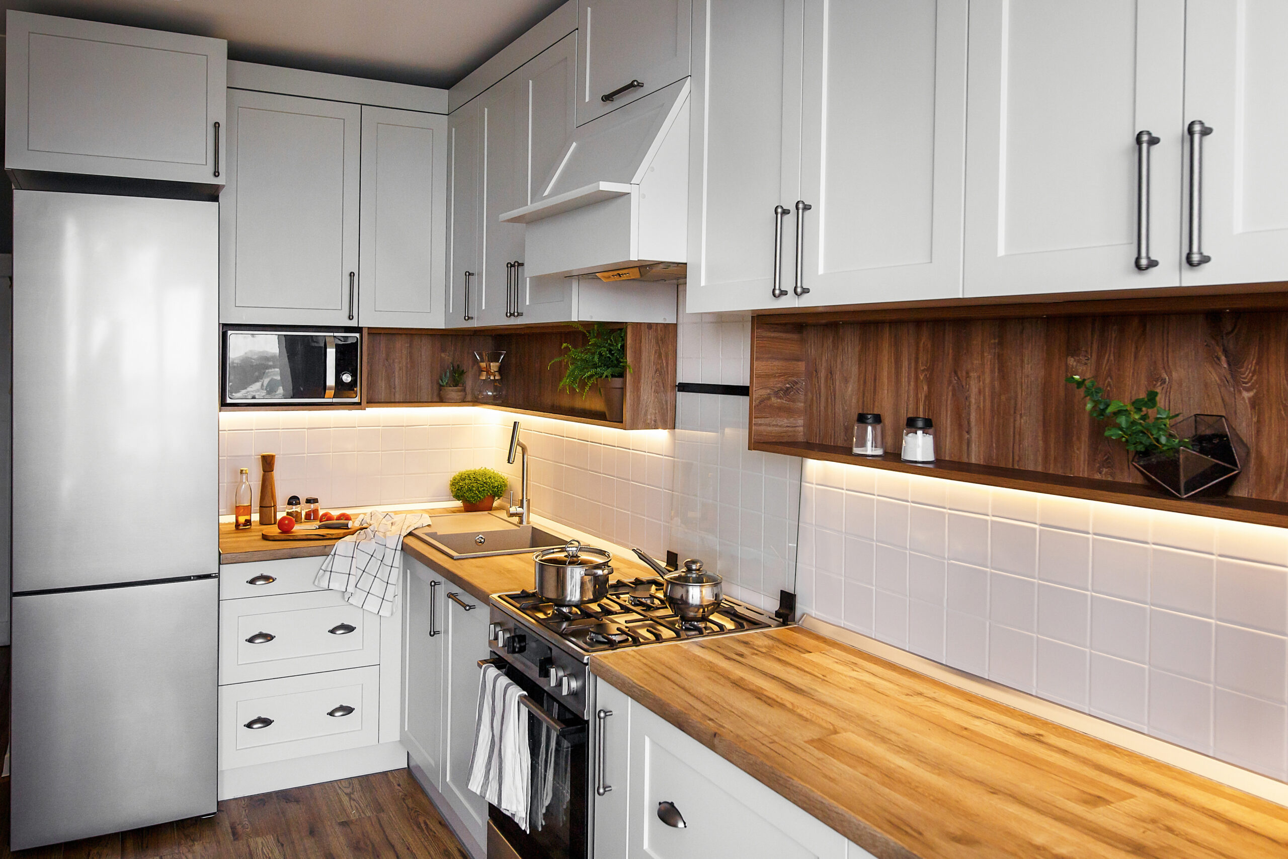 Stylish light gray kitchen interior with modern cabinets and stainless steel appliances in new home. kitchen design in scandinavian style. green plants decor, wooden worktop, sink